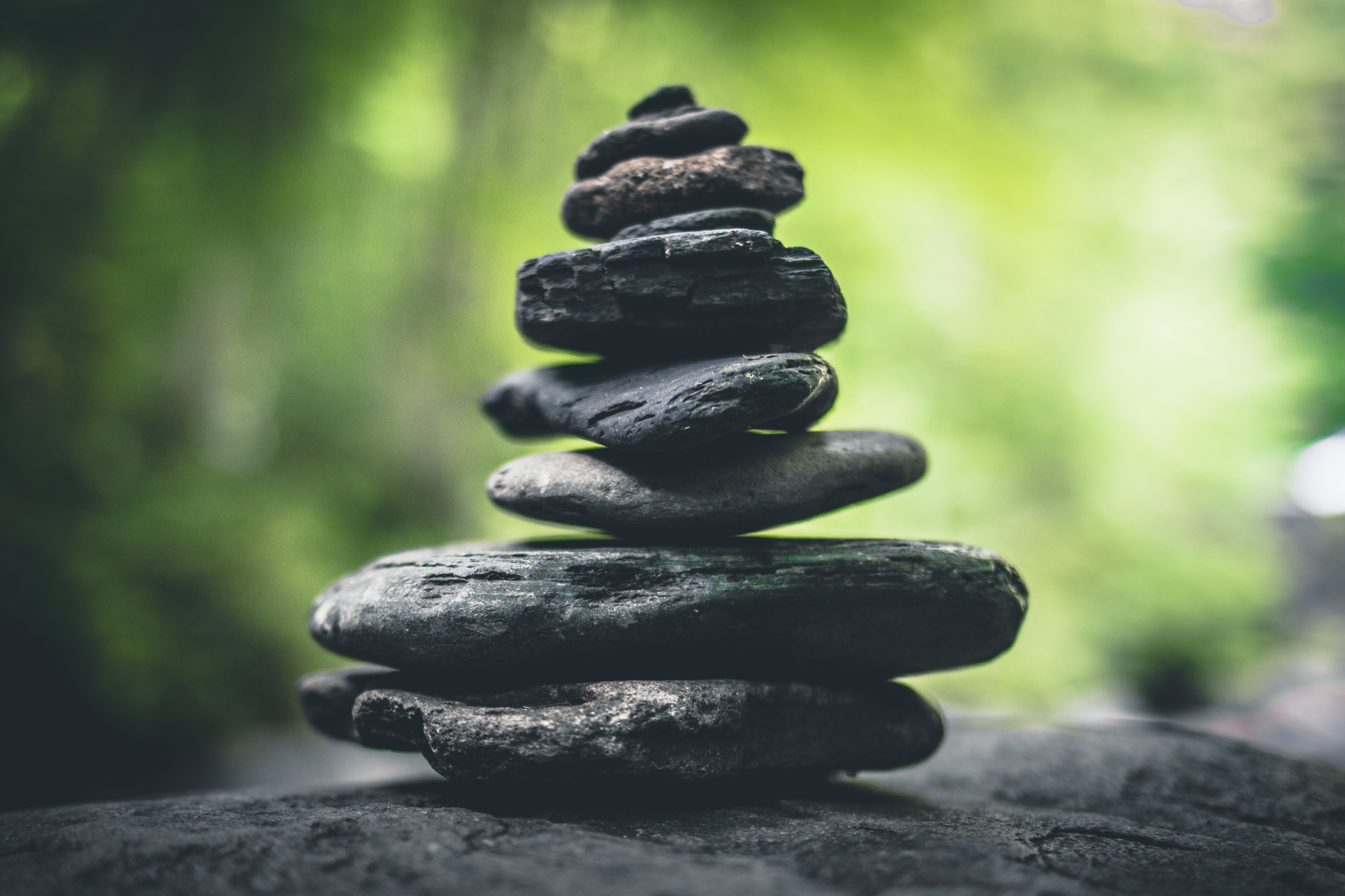 Stack of balanced grey rocks, with blurry greenery in the background.